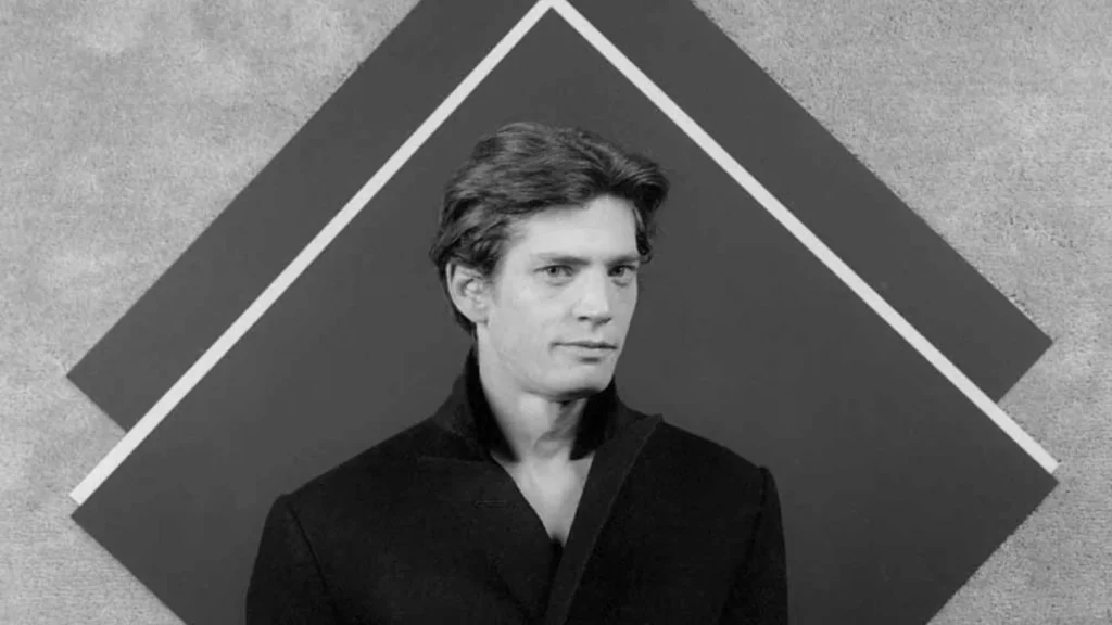 Retrato en blanco y negro de un hombre frente a una composición geométrica minimalista, estilo fotográfico de estudio con estética clásica.