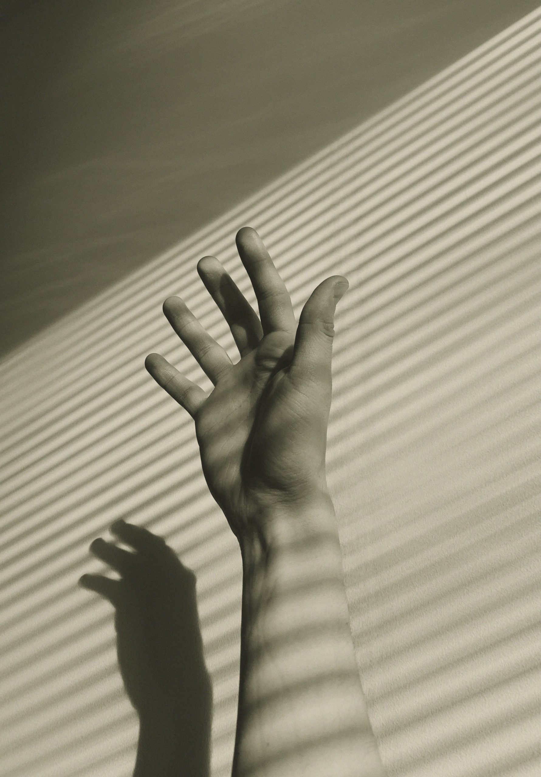Una mano entre luces y sombras de persiana
