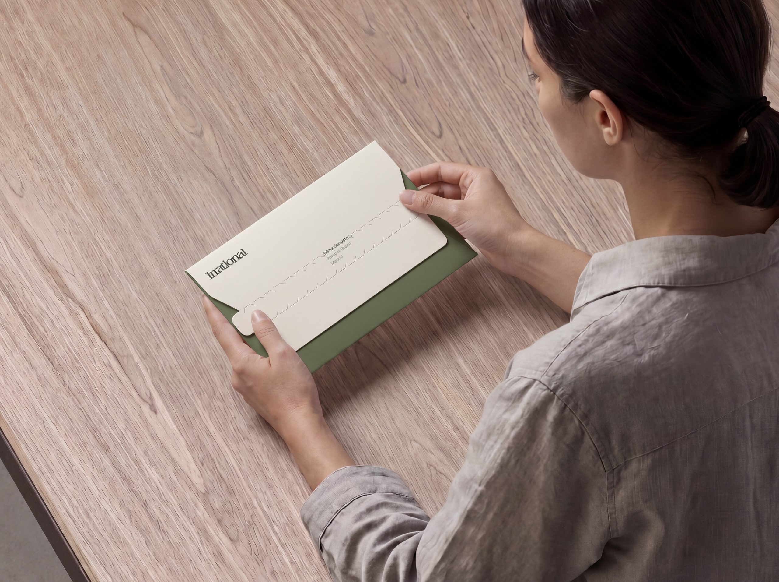 Sobre de Irrational en manos de una persona sobre una mesa de madera